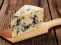 Ein Stück Blauschimmelkäse, perfekt für eine cremige blue cheese sauce, liegt auf einem Holzbrett.