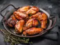 Saftige Hähnchenflügel in einer glänzenden Marinade, garniert mit frischem Thymian, serviert auf einer dunklen Platte.