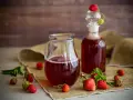 Frischer Erdbeersirup in Karaffe und Flasche, umgeben von reifen Erdbeeren. Perfekt, um Erdbeersirup selber machen.