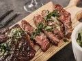 Saftiges, in Scheiben geschnittenes Flank Steak mit Kräutern und einer grünen Sauce auf einem Holzbrett serviert.
