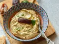 Cremiger Dattel Dip in einer bunten Schale, garniert mit einer Dattel und Petersilie. Dazu Brot und weitere Datteln auf einem Holzbrett.