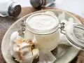 Frische Knoblauchsauce selber machen: cremige Sauce im Glas mit Knoblauchzehen und Salzstreuer im Hintergrund.