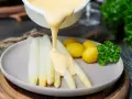 Sauce Hollandaise wird über weißen Spargel und Kartoffeln gegossen, um das Gericht zu verfeinern.