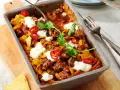 Herzhafter Shepherd's Pie mit Hackfleisch, Tortilla-Chips, Chili-Ringen und Klecksen saurer Sahne, garniert mit Koriander.