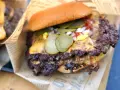 Saftiger Smash Burger mit geschmolzenem Käse, Gurken, Zwiebeln und Ketchup auf einem Brötchen, eingewickelt in Papier.