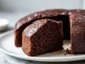 Saftiger Schokoladenkuchen, frisch aus dem Airfryer, auf einer weißen Platte. Ein Stück ist bereits angeschnitten.