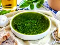 Frisches, grünes Pesto ohne Pinienkerne in einer Schüssel, daneben Knoblauch, Brot und Parmesan.