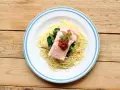 Ein Teller mit One Pot Lachs Pasta, garniert mit Petersilie und Tomatensauce, daneben Spargel und Spinat auf einem Holztisch.