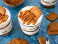 Schichtdessert im Glas: cremiges Lotus Cheesecake mit Keksbröseln und Karamellsoße, garniert mit einem Lotus Keks.