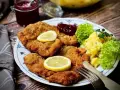 Ein köstlicher **Garnitur Wiener Schnitzel** mit Kartoffelsalat, Preiselbeeren und Zitrone auf einem Teller.