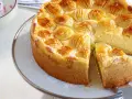 Ein köstlicher, schneller Apfelkuchen mit Schmand und Pudding, verziert mit Apfelscheiben und Puderzucker. Daneben eine Schüssel mit Beeren-Sahne.