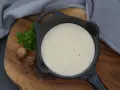 Cremige Béchamelsauce in einer kleinen Gusseisenpfanne, garniert mit Petersilie und Muskatnüssen.