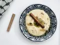Cremiger Hummus, selbst gemacht, mit Zimtstange und Knoblauch garniert auf einem blau-weißen Teller.
