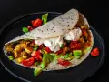 Saftige Fajitas de pollo mit Hähnchen, Gemüse, Avocado und einem Klecks Sauerrahm auf einem Tortilla-Wrap.