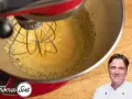 Küchenmaschine mixt eine cremige, gelbe Masse, die an Sauce Hollandaise erinnert. Ein Koch lächelt im Vordergrund.
