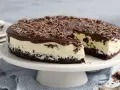 Eine köstliche Bananensplit Torte ohne Backen, mit Schokoladenüberzug und Schokostreuseln. Ein Stück ist bereits angeschnitten.