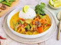 Ein bunter Thai Curry ohne Kokosmilch mit Reis, Paprika, Zucchini und Pilzen, garniert mit Limette und Koriander.