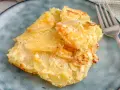 Ein Stück Kartoffelgratin einfach mit Sahne, goldbraun gebacken, auf einem blauen Teller. Daneben eine Gabel.