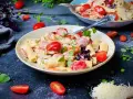 Cremige One Pot Pasta mit Würstchen, Erbsen und Kirschtomaten, garniert mit frischen Kräutern und geriebenem Käse.