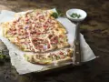 Flammkuchen mit Speck und Zwiebeln, eine klassische Idee für Flammkuchen Belag. Frisch und knusprig auf Holz serviert.