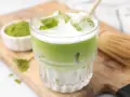 Erfrischender Matcha Latte mit Eis, Milch und einem Hauch von Starbucks-Rezept-Magie. Daneben eine Schale Matcha-Pulver und ein Chasen.