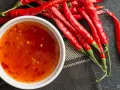 Frische rote Chilis neben einer Schüssel mit selbstgemachter Chili-Sauce. Perfekt zum Chili Sauce selber machen!