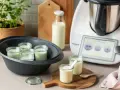 Kleine Gläser mit Joghurt in einem Dampfgarer, bereit, trinkjoghurt selber machen. Daneben ein Thermomix und Milchflasche.