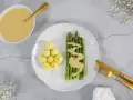 Spargel mit kleinen Kartoffeln und einer cremigen, veganen Sauce Hollandaise. Ein goldener Löffel liegt in der Sauce.