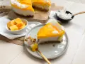 Ein cremiges Mango Cheesecake ohne Backen, garniert mit Kokosflocken. Ein Stück wird gerade mit einem Löffel probiert.