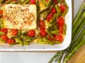 Spargel, Kirschtomaten und Pasta mit einem Block Feta, gewürzt mit Kräutern, in einer Auflaufform.