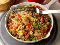 Reis mit Hackfleisch, Erbsen, Mais und Paprika in einer Schüssel, serviert mit einer Gabel.