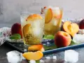 Erfrischender Pfirsich Eistee selber machen: Gläser mit Eis, Pfirsichspalten und sprudelndem Tee. Frische Pfirsiche und Minze daneben.