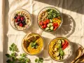 Vier Schüsseln mit gesunden, vorbereiteten Gerichten: Haferflocken mit Früchten, Quinoa-Salat, Linsencurry mit Naan und Curry mit Reis. Perfekt für Meal Prep!