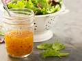 Ein Glas mit selbstgemachtem Salatdressing, das aussieht wie im Restaurant. Daneben ein Sieb mit frischem Salat.