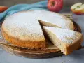 Ein schneller, saftiger Kuchen mit Apfelmus, bestäubt mit Puderzucker. Ein Stück wird gerade herausgenommen.