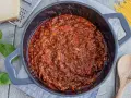 Herzhaftes Bolognese-Rezept original in einem Topf, mit frischem Basilikum, Parmesan und Spaghetti daneben.