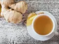Frischer Ingwer und eine Tasse Ingwertee auf Holzhintergrund. Vielleicht ein kleiner Fehler bei der Zubereitung, wenn der Tee zu stark ist.