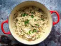 Cremiges Pilzrisotto in rotem Topf, garniert mit Schnittlauch.