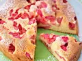 Ein saftiger Erdbeer Rhabarber Kuchen, bestäubt mit Puderzucker, wird auf einem Teller präsentiert. Ein Stück ist bereits herausgeschnitten.