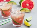 Erfrischender Aperol Paloma mit Grapefruit und Limette, serviert mit Eis und grünen Trinkhalmen.