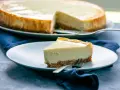 Ein Stück cremiger american cheesecake mit knusprigem Boden auf einem Teller, daneben ein ganzer Kuchen.