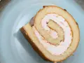 Ein Stück Biskuitrolle mit 5 Eiern und rosa Füllung auf einem blauen Teller.