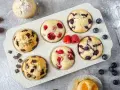 Leckeres Muffins Rezept: Schoko-, Himbeer- und Blaubeermuffins in einer Form, daneben frische Beeren und Schokostückchen.