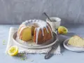 Ein saftiger Zitronenkuchen mit Zuckerguss, perfekt für ein Lemon Drizzle Cake Rezept. Daneben liegen frische Zitronen und ein Stück Kuchen.