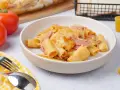 Herzhaftes Rigatoni al Forno mit Schinken und geschmolzenem Käse in einer Schüssel, daneben Tomaten und Brot.