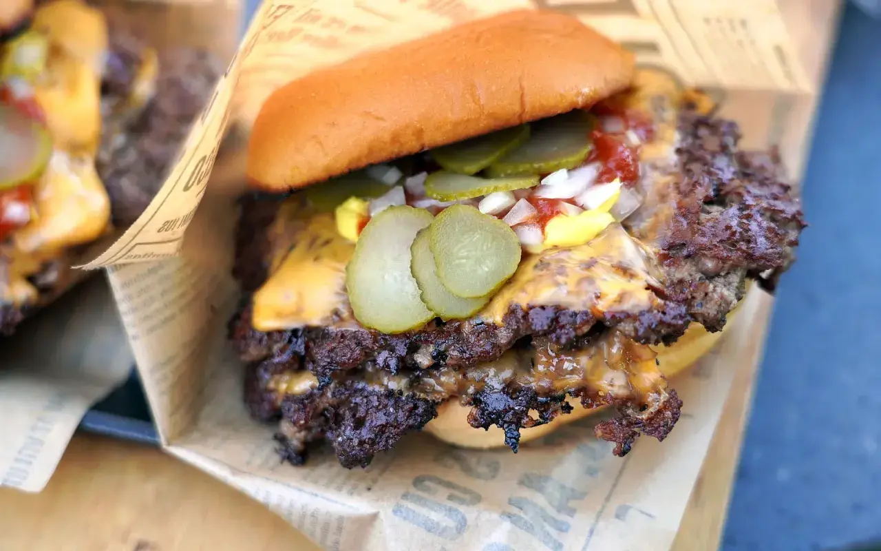 Saftiger Smash Burger mit geschmolzenem Käse, Gurken, Zwiebeln und Ketchup auf einem Brötchen, eingewickelt in Papier.