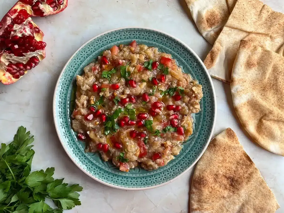 Baba ganoush, ein cremiger Auberginen-Dip, garniert mit Granatapfelkernen und Petersilie, serviert mit Pitabrot.