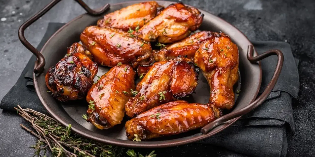 Saftige Hähnchenflügel in einer glänzenden Marinade, garniert mit frischem Thymian, serviert auf einer dunklen Platte.