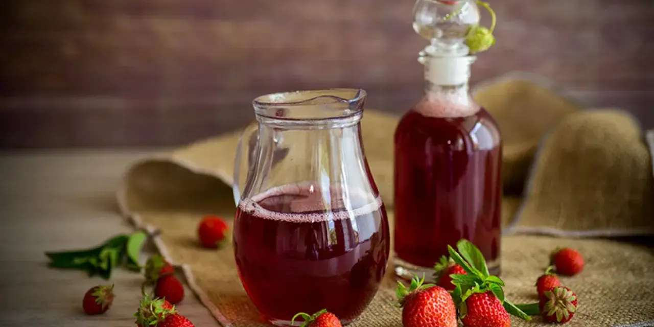 Frischer Erdbeersirup in Karaffe und Flasche, umgeben von reifen Erdbeeren. Perfekt, um Erdbeersirup selber machen.
