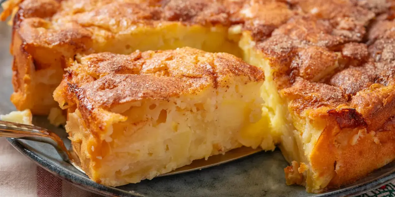 Ein saftiger apfelkuchen mit schale, goldbraun gebacken und mit Zimt bestreut. Ein Stück wird gerade herausgehoben.